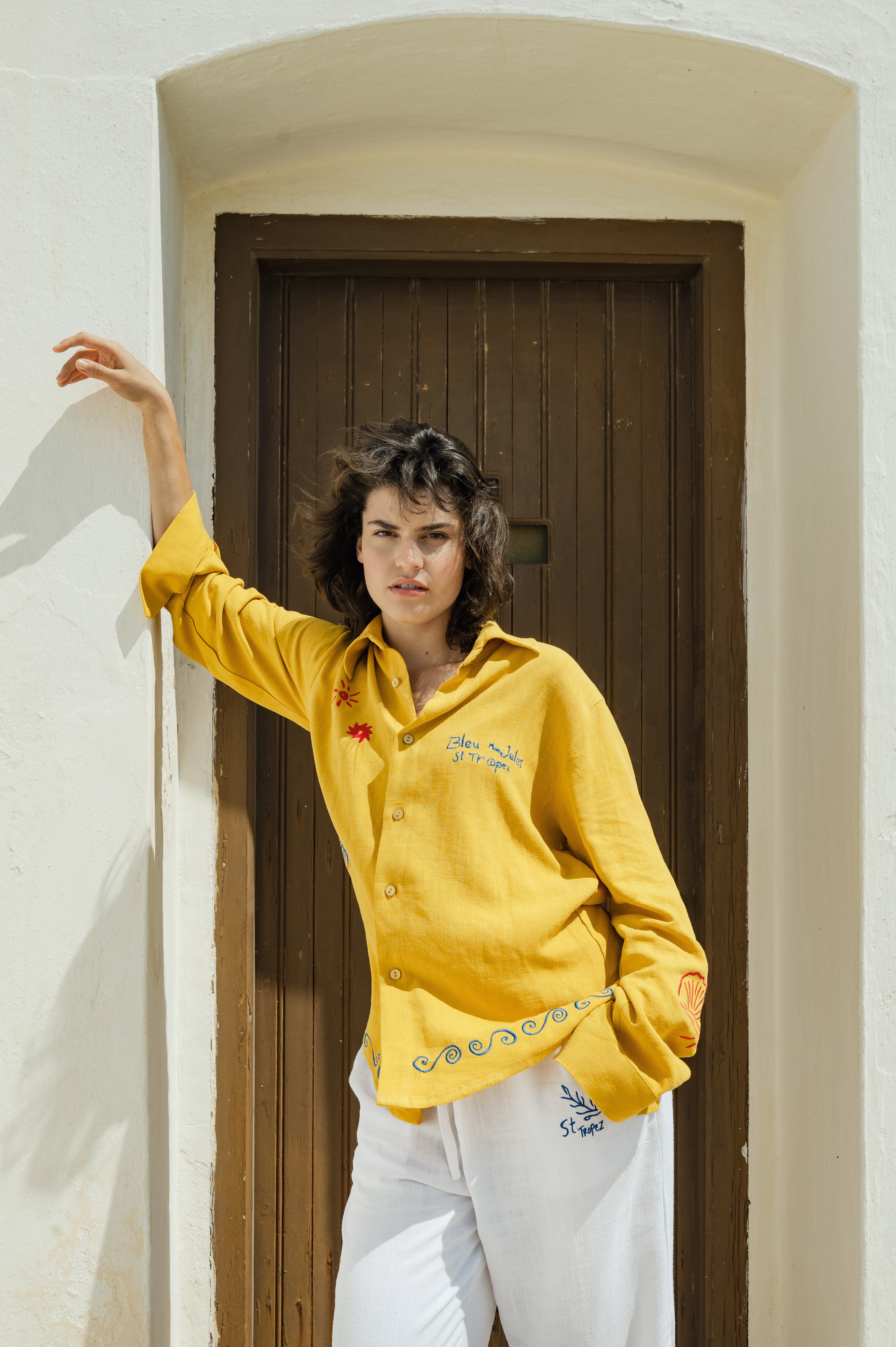 Femme en chemise jaune soleil Chemise fluide couleur miel, portée sur un pantalon blanc, allure libre et joyeuse sous le soleil.