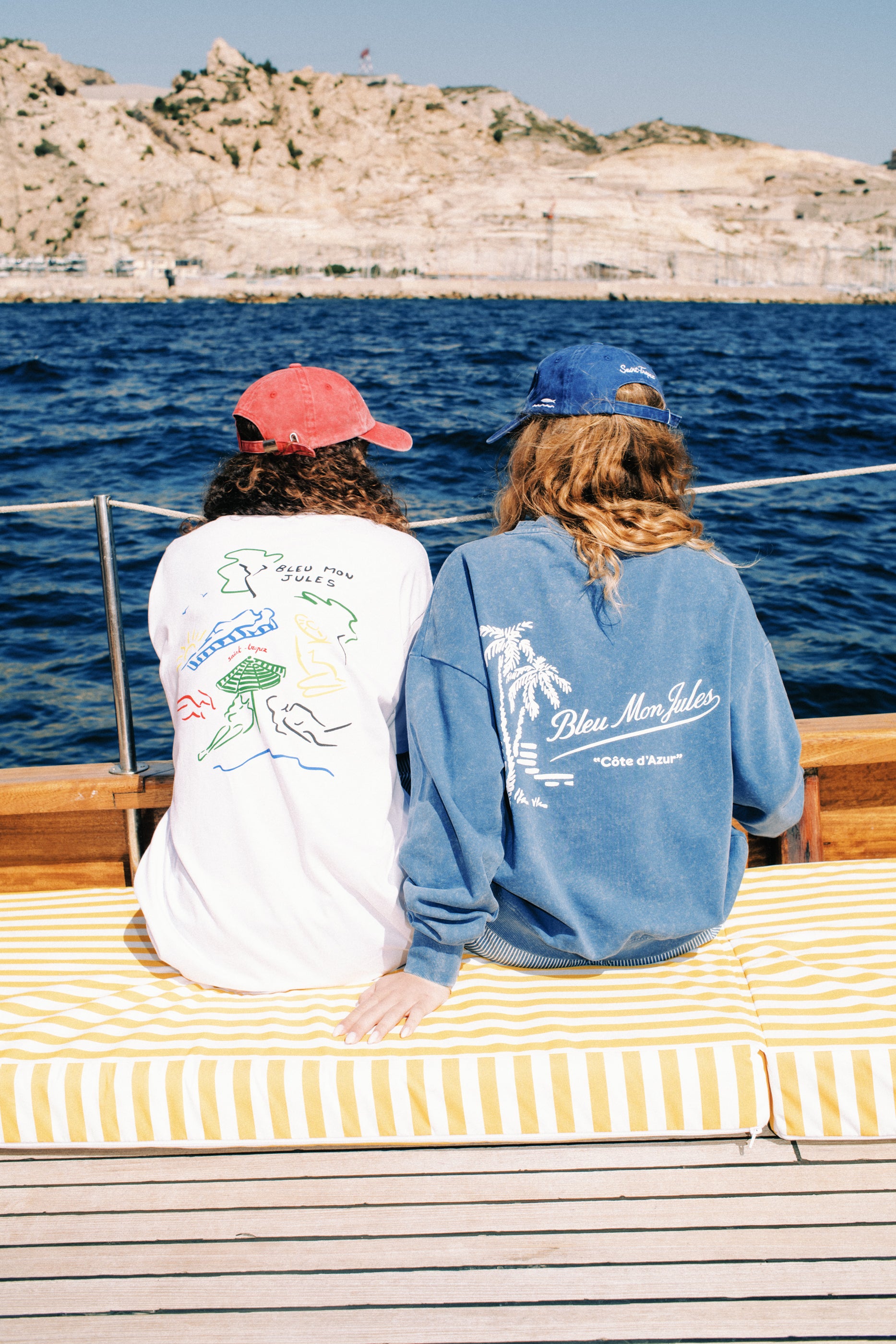 Deux personnes en sweat Palmier Délavé bleu lavé sur bateau face à la côte méditerranéenne, collection Côte d'Azur