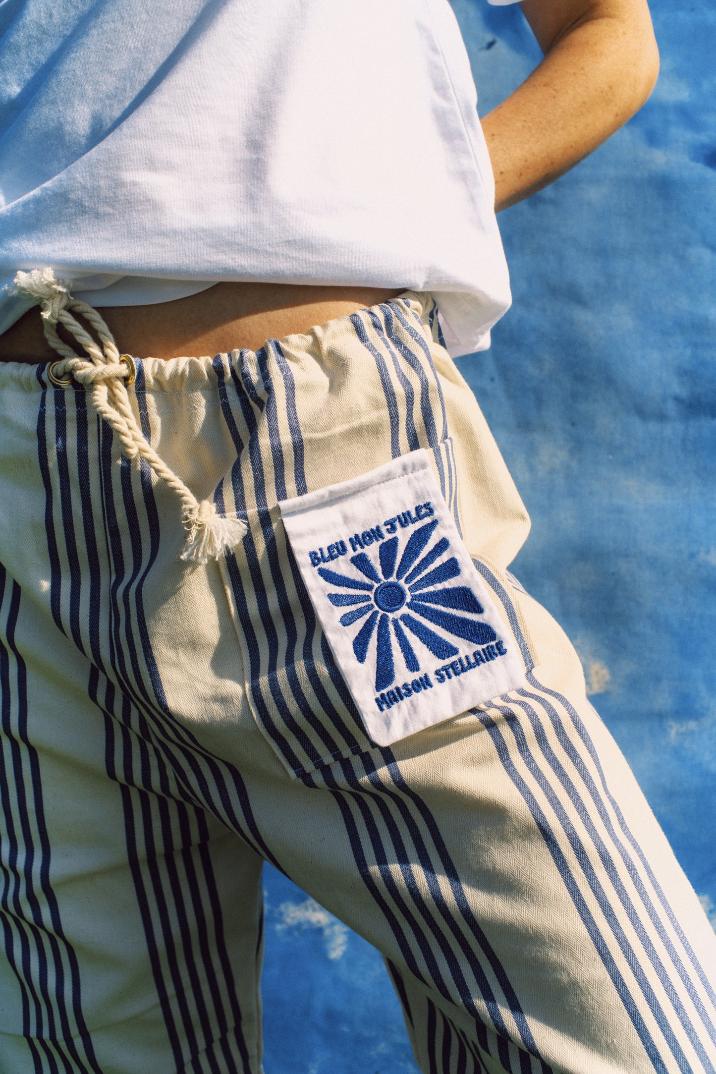 Détail de la broderie sur le pantalon porté – Gros plan sur la broderie bleue du pantalon, motif graphique inspiré du sud.
