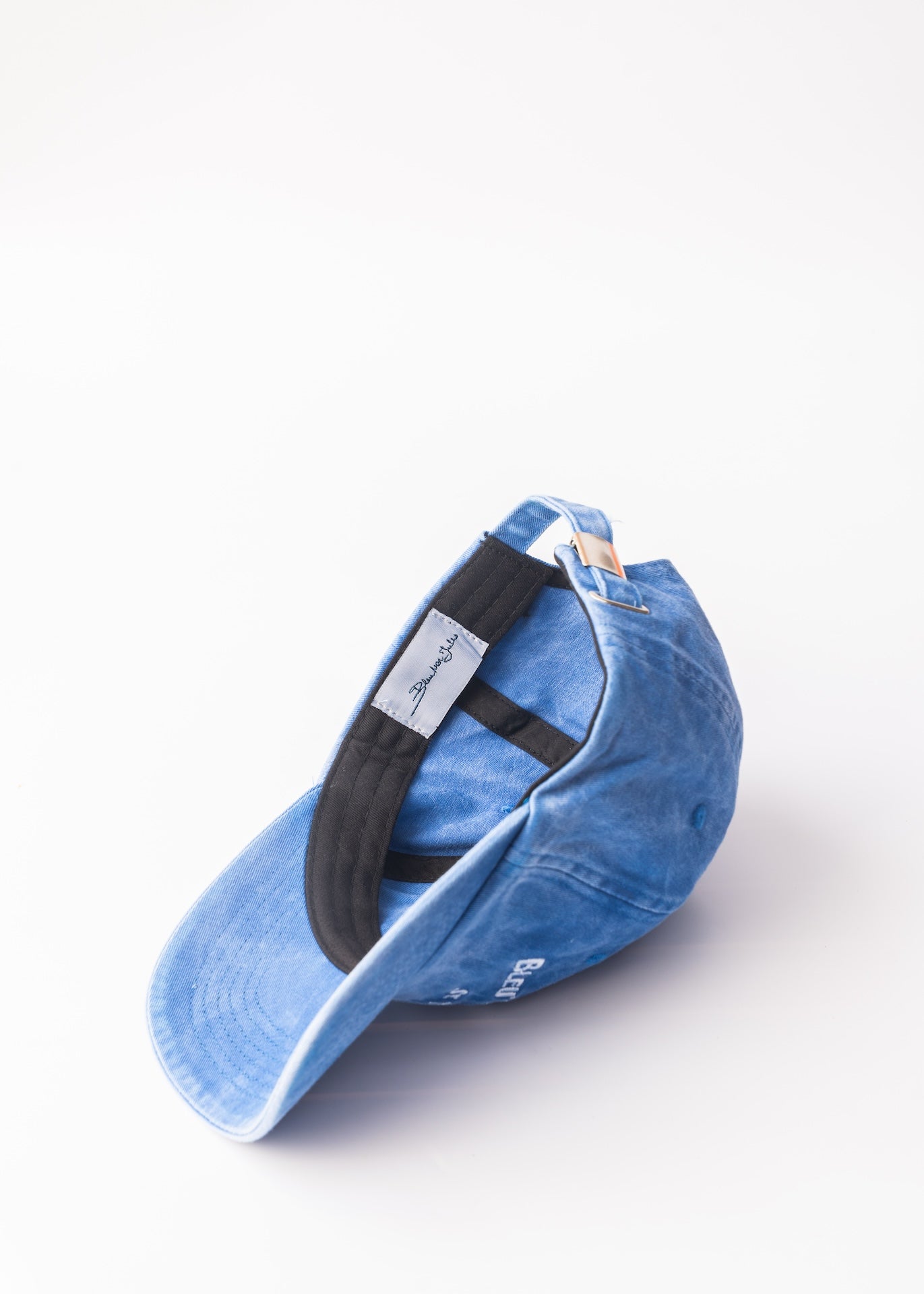 Casquette bleue délavée – vue inclinée Casquette bleu clair légèrement usée, détails brodés et visière courbée pour un look vintage marin.