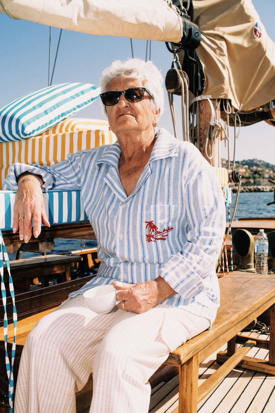 Homme portant pantalon cargo rayé rouge et écru avec broderie Bleu mon Jules, assis sur voilier en mer