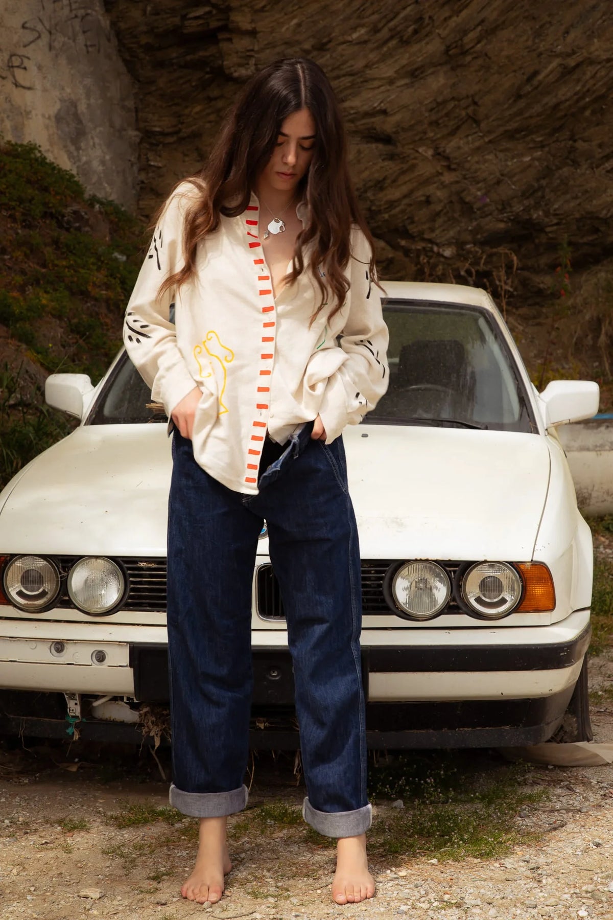 Femme en veste beige brodée et jean bleu clair devant voiture vintage blanche rétro
