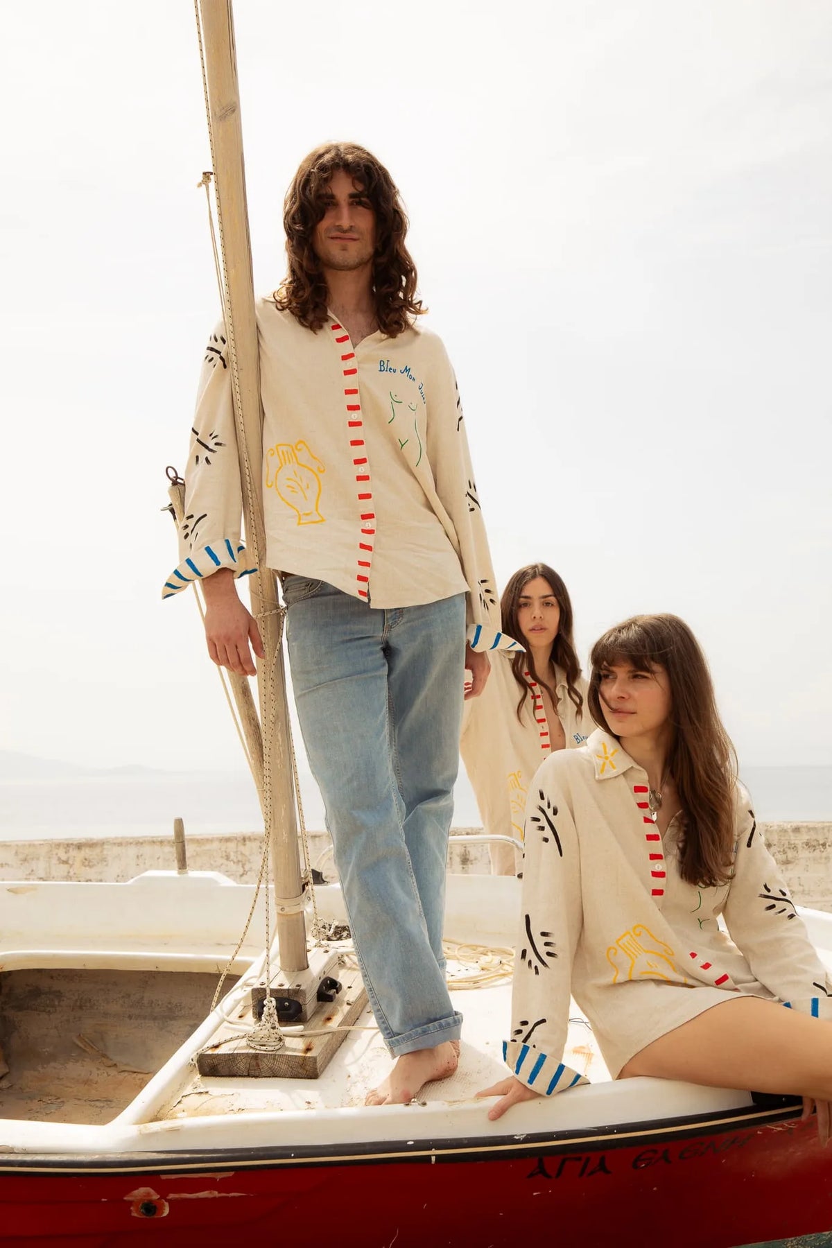 Trois personnes portant des pulls beige à motifs colorés posent sur un voilier face à la mer