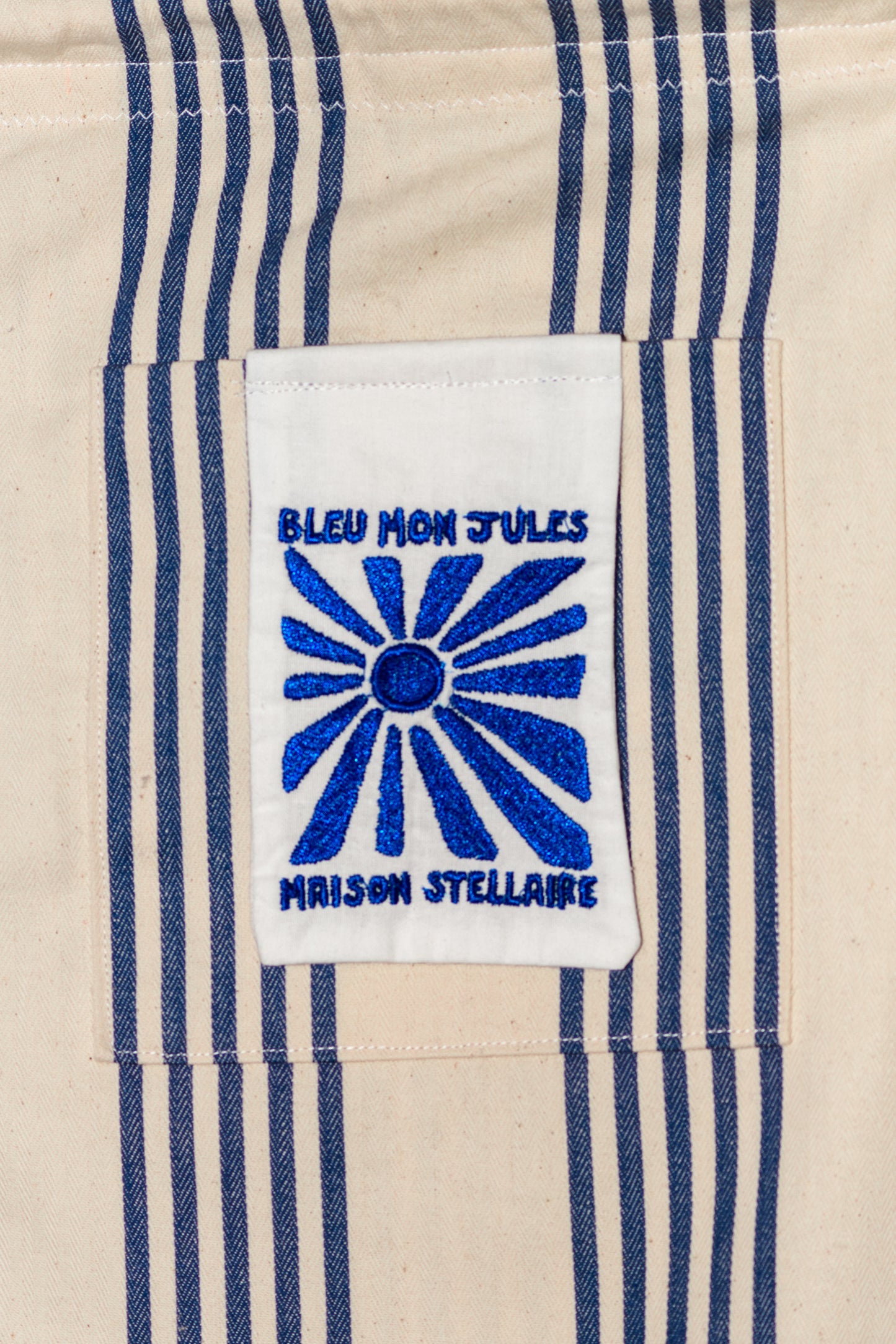 Détail de la poche brodée – Zoom sur la broderie bleue inspirée du motif marin, sur fond de tissu rayé beige et bleu.