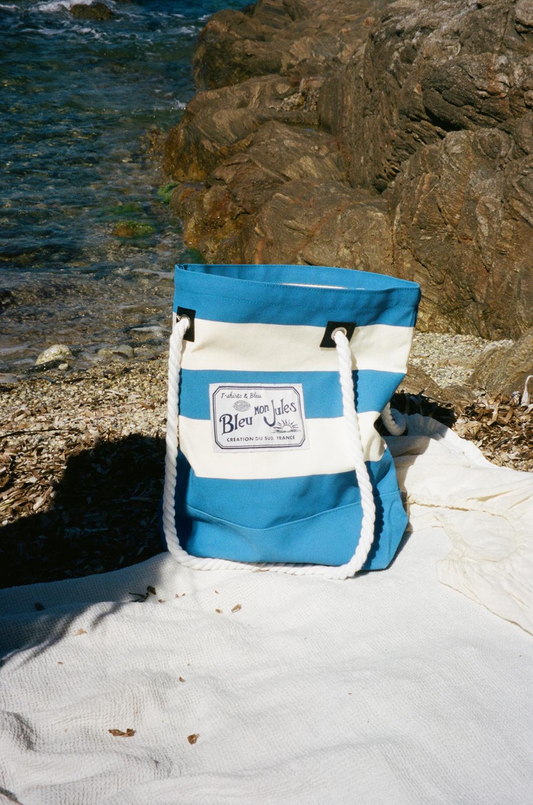 Sac de plage rayé bleu et écru Cabas avec anses corde posé sur la plage rocheuse méditerranéenne